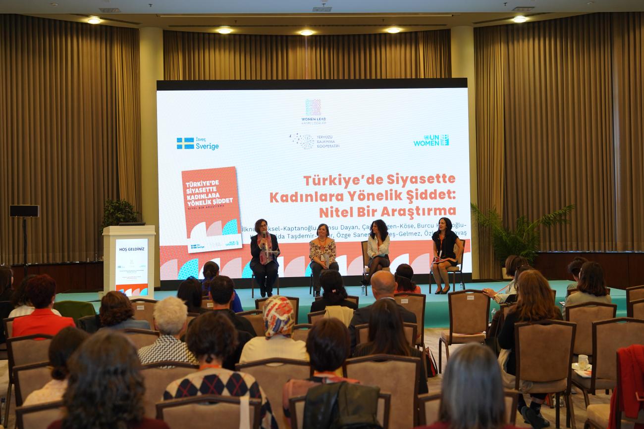 Perde önünde 4 panelist oturuyor. Karşılarında dinleyiciler var. Perde'de Türkiye'de Siyasette Kadınlara Yönellik Şİddet: Nitel bir araştırma yazıyor. 