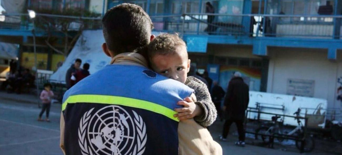 Yüzünde son derece korkmuş ifadesiyle bir küçük çocuk BM yardım görevlisi tarafından kucakta taşınıyor. 