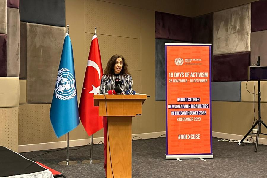 Uluslararası Göç Kuruluşu Misyon Şefi Yardımcısı Claudia Natali kürsüde konuşma yapıyor. Arkasında BM ve Türk bayrağı var. 