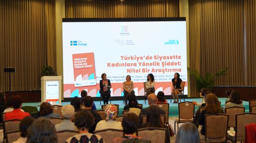 Perde önünde 4 panelist oturuyor. Karşılarında dinleyiciler var. Perde'de Türkiye'de Siyasette Kadınlara Yönellik Şİddet: Nitel bir araştırma yazıyor. 