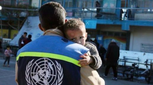 Yüzünde son derece korkmuş ifadesiyle bir küçük çocuk BM yardım görevlisi tarafından kucakta taşınıyor. 