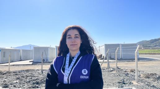Seda Karakuş in front of a container city wearing a blue vest with OXFAM logo